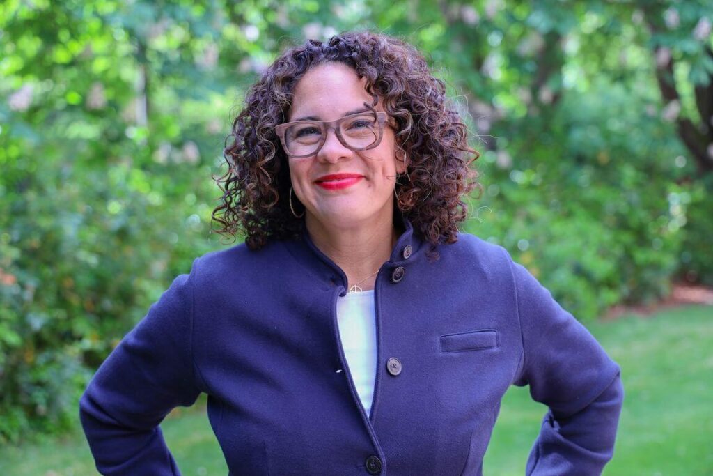 Vice Provost for Inclusive Excellence Ralina Joseph smiling, in an outdoor area surrounded by greenery