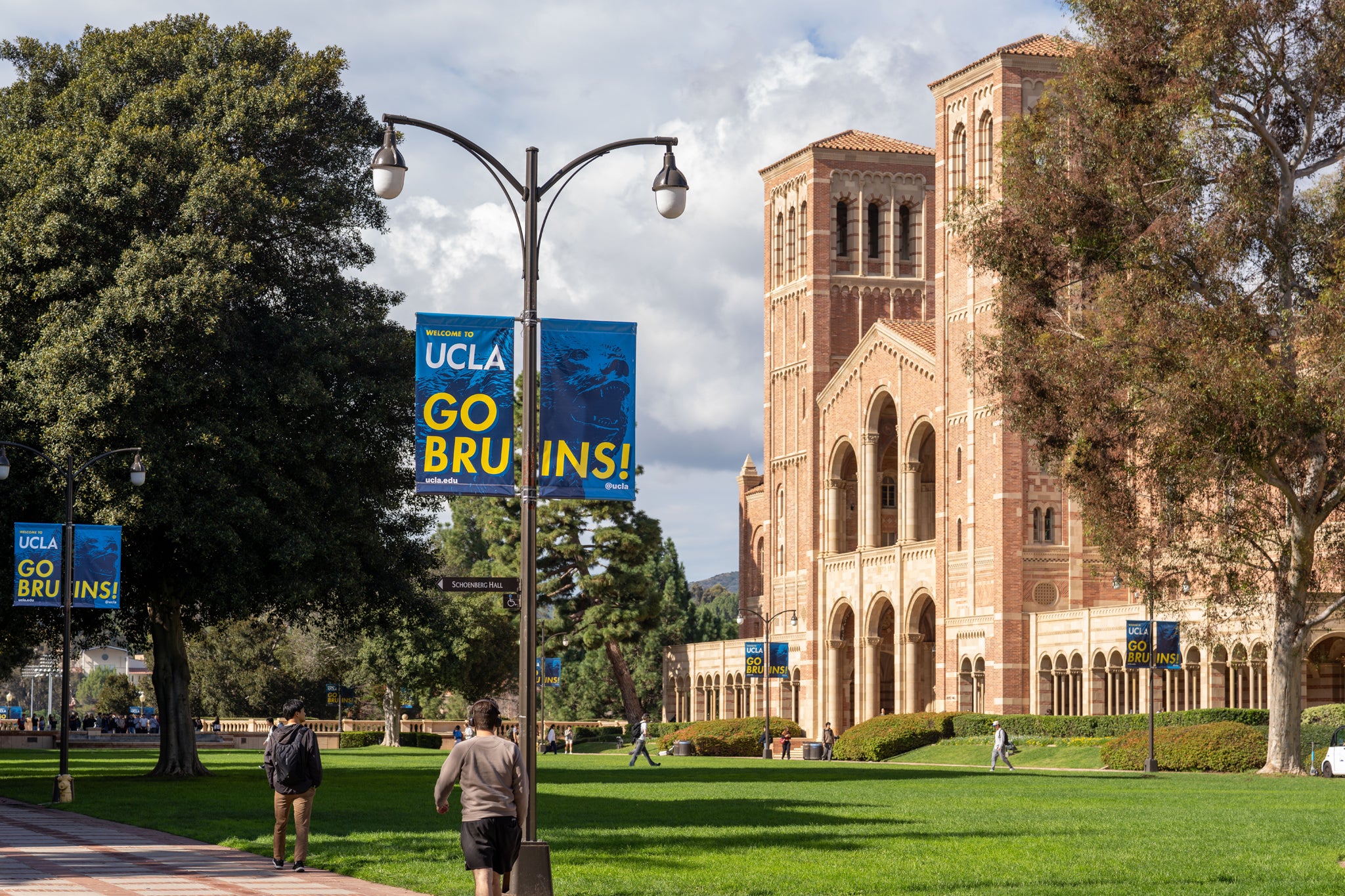 People walking on UCLA campus with Royce Hall on the left-hand side, punctuated by "Go Bruins!" banners on lampposts