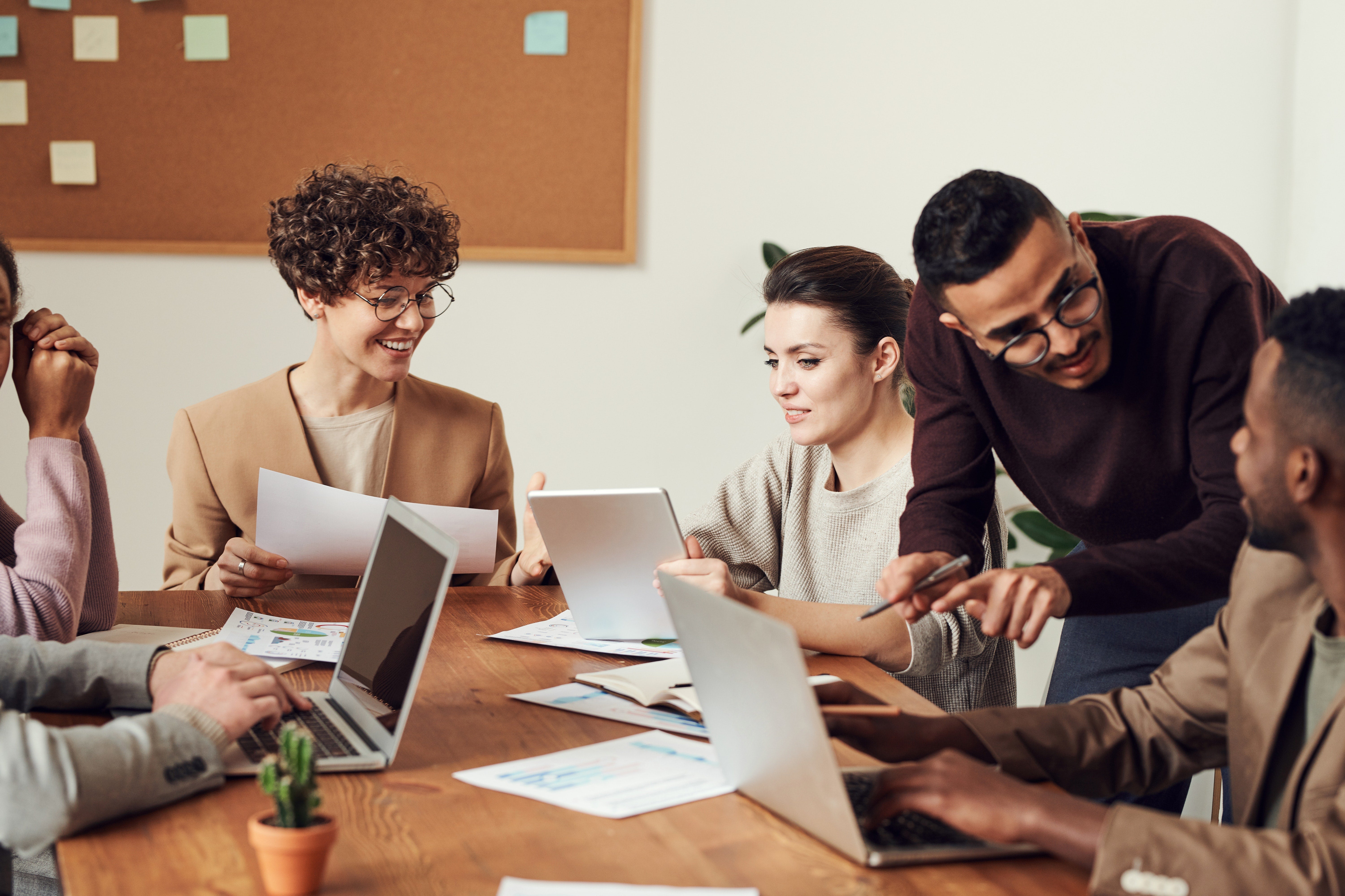 diverse group of colleagues in an office space collaborate on a desk, with laptops and papers surrounding them