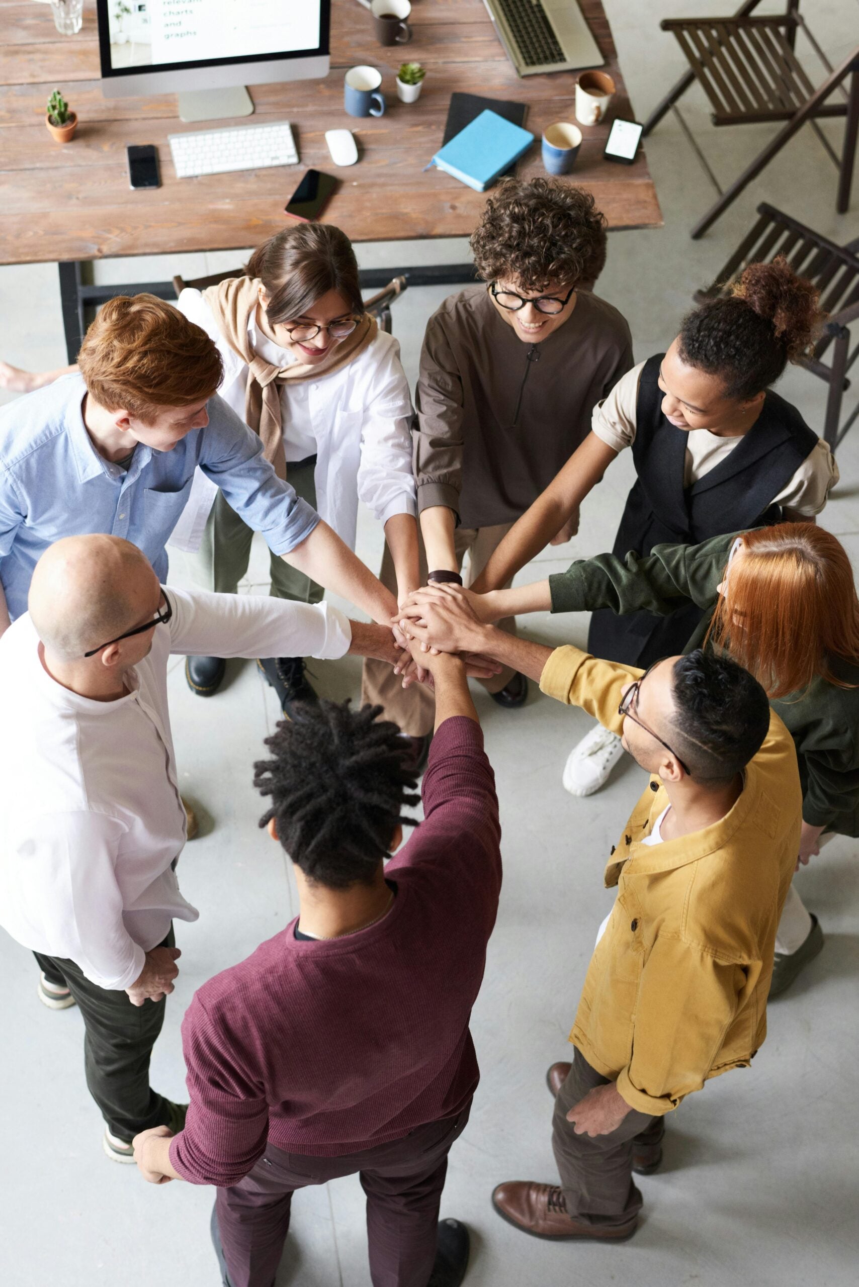diverse group of colleagues in an office space, all bringing in their hands together in solidarity