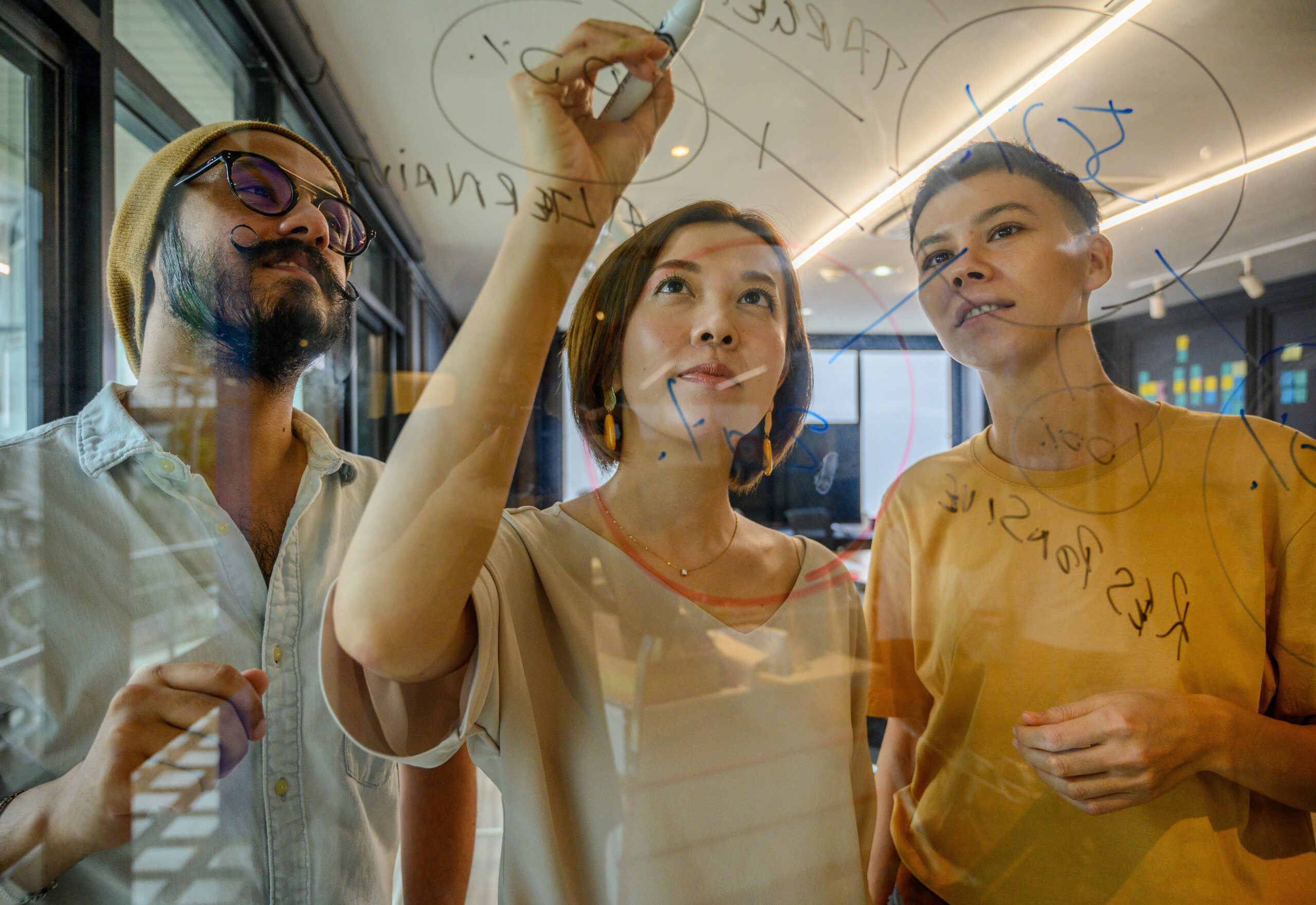 diverse group of colleagues in an office space look at a glass writing surface with writing on it